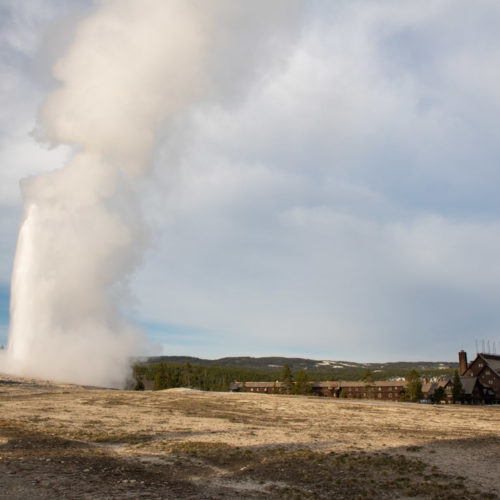 Old Faithful eruption in morning light with Old Faithful Inn, Yellowstone National Park