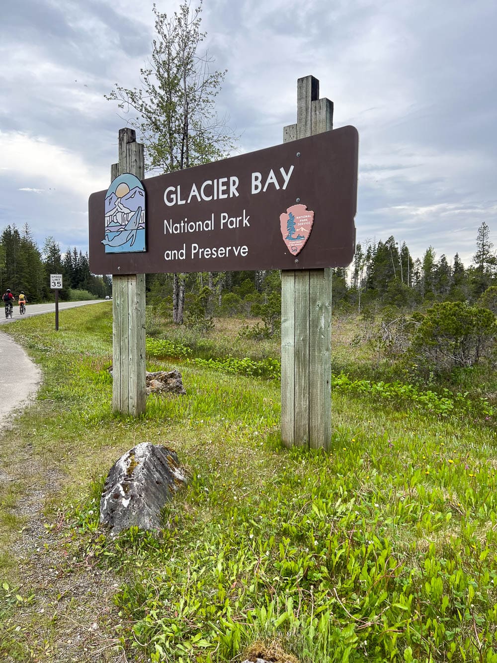 A couple of cyclists pedal past the Glacier Bay National Park entrance sign on the road between Gustavus and Bartlett Cove - Image credit: Bram Reusen